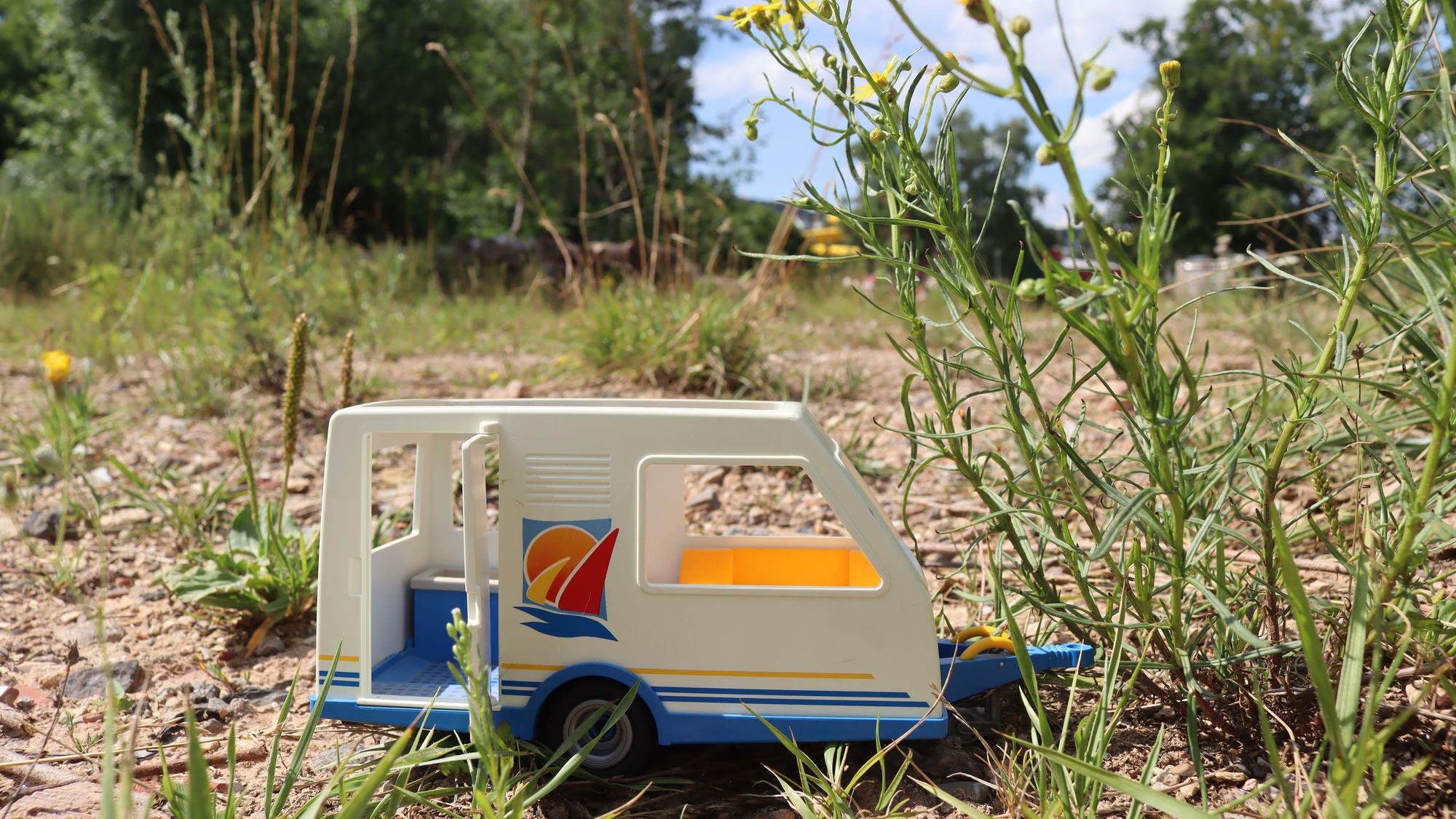 Ein kleiner Spielzeug-Wohnwagen steht auf einem leeren Feld zwischen ein paar Pflanzen in Bad Münstereifel.
