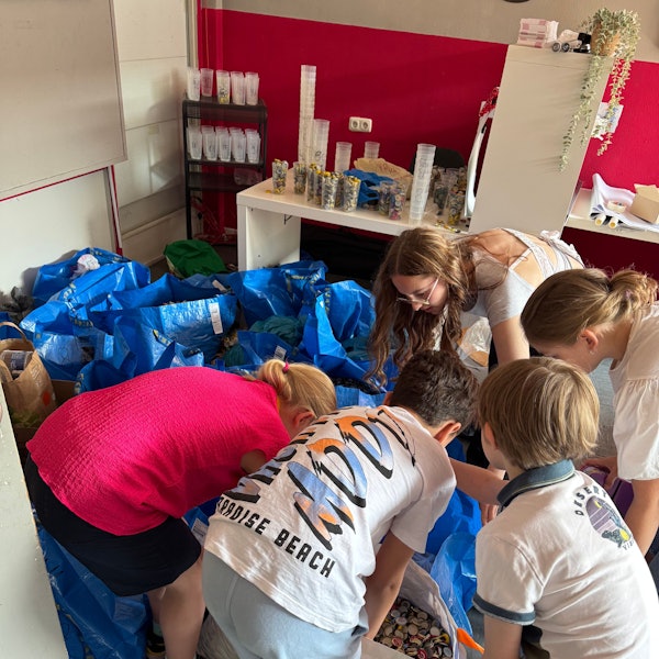 Auf dem Bild sind Kinder zu sehen, die Kronkorken in große blaue Säcke sortieren.