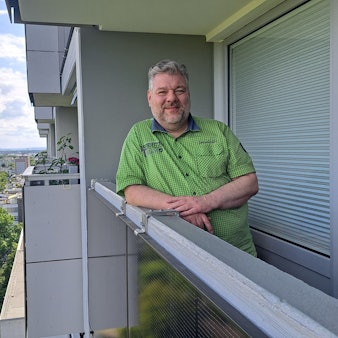 Ein Mann lehnt an der Brüstung seines Balkons, an dem ein Solarmodul angebracht ist.