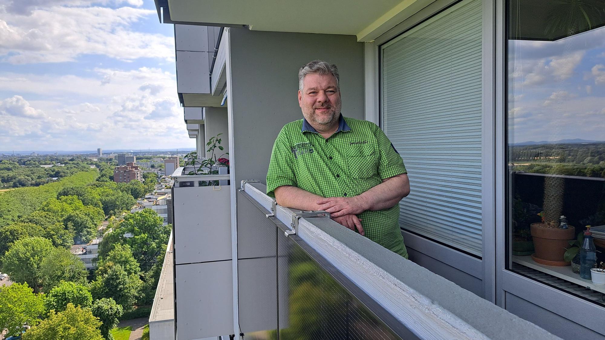 Ein Mann lehnt an der Brüstung seines Balkons, an dem ein Solarmodul angebracht ist.