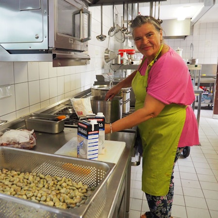 Monika Bärhausen trägt ein pinkes Shirt und eine grüne Schürzte. Sie arbeitet am Herd in der Küche der Gaststätte Watteler im Freilichtmuseum Kommern.