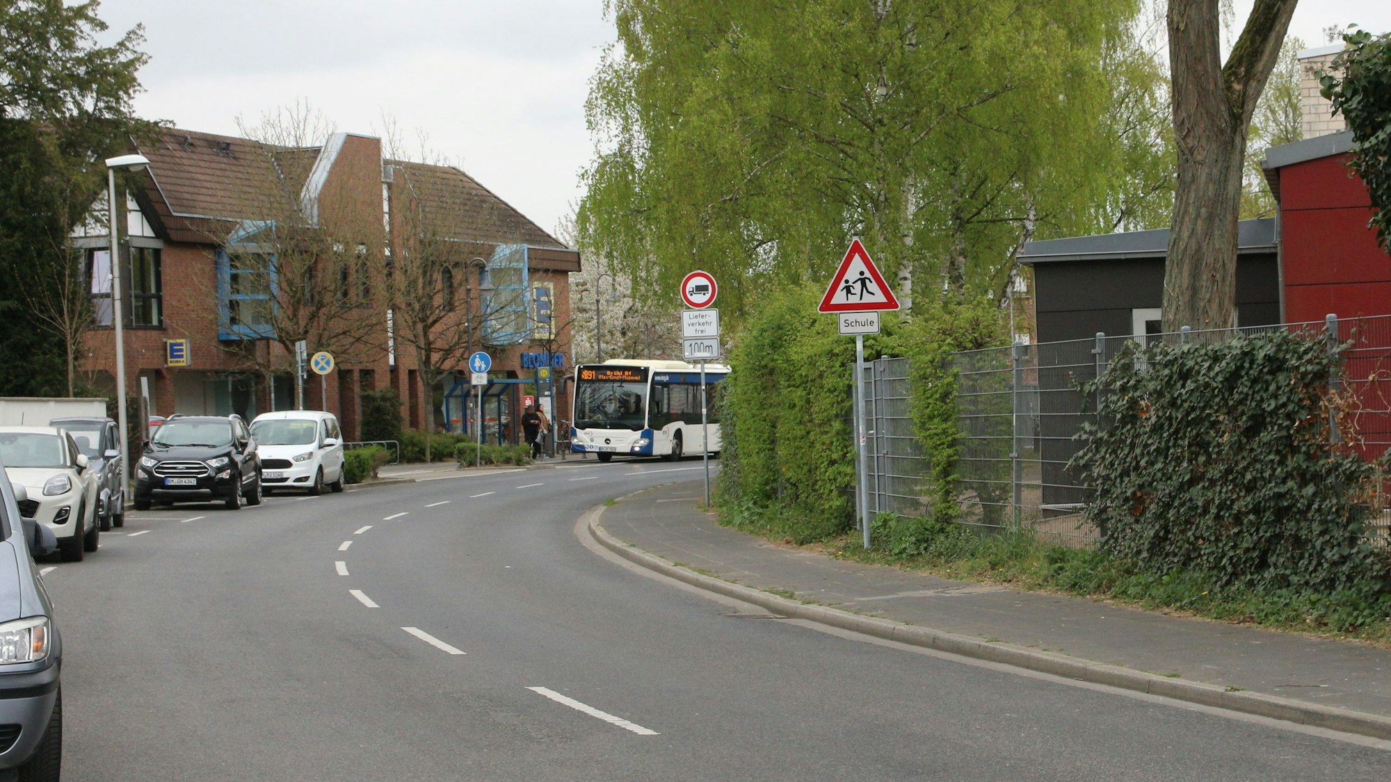 Zu sehen ist eine Straße, an der Autos parken, im Hintergrund hält ein Bus.