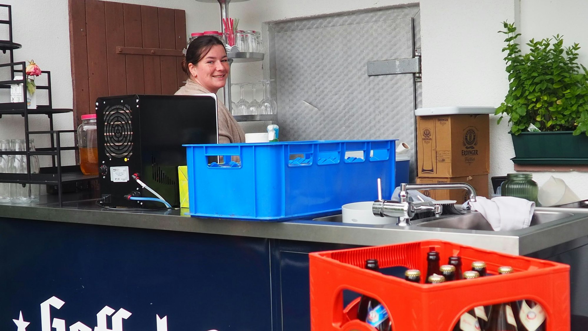 Joanna Bärhausen steht an einer Theke, auf der eine Zapfanlage steht. Vorne sind Bierkästen zu erkennen.