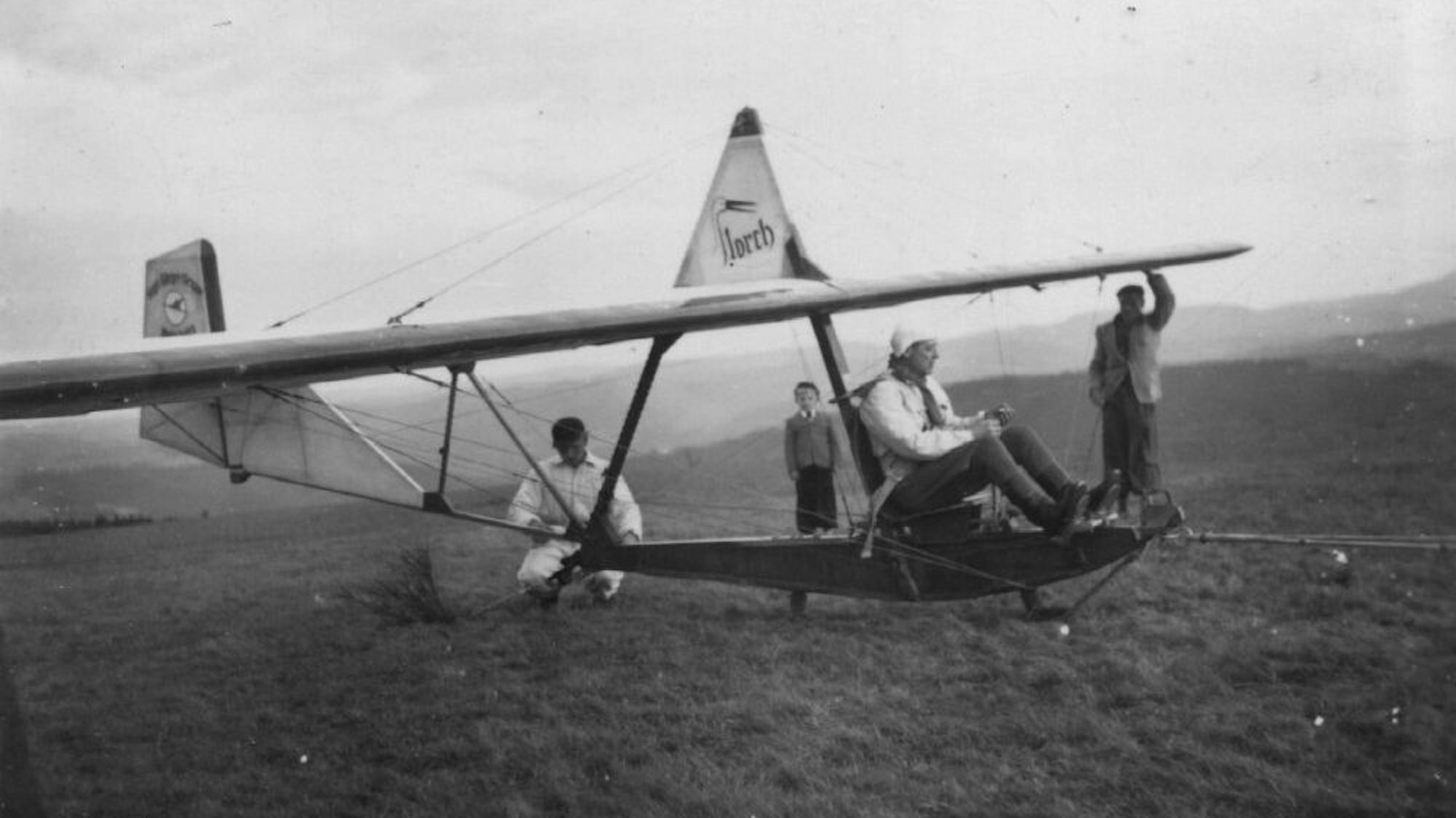 Schwarzweiß-Aufnahme eines Segelflugzeugs aus den 1950er Jahren. Ein Storchenkopf ist als S im Wort „Storch“ auf dem Flieger zu sehen.