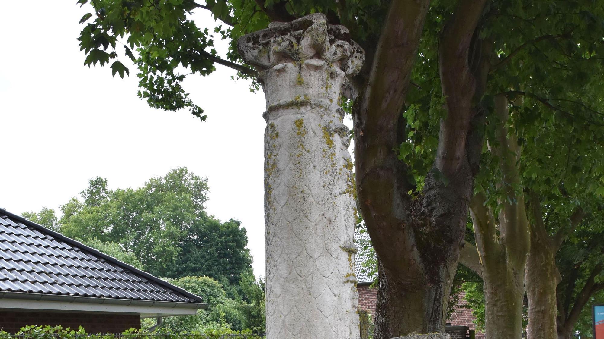 Zu sehen ist eine graue Säule vor Bäumen.