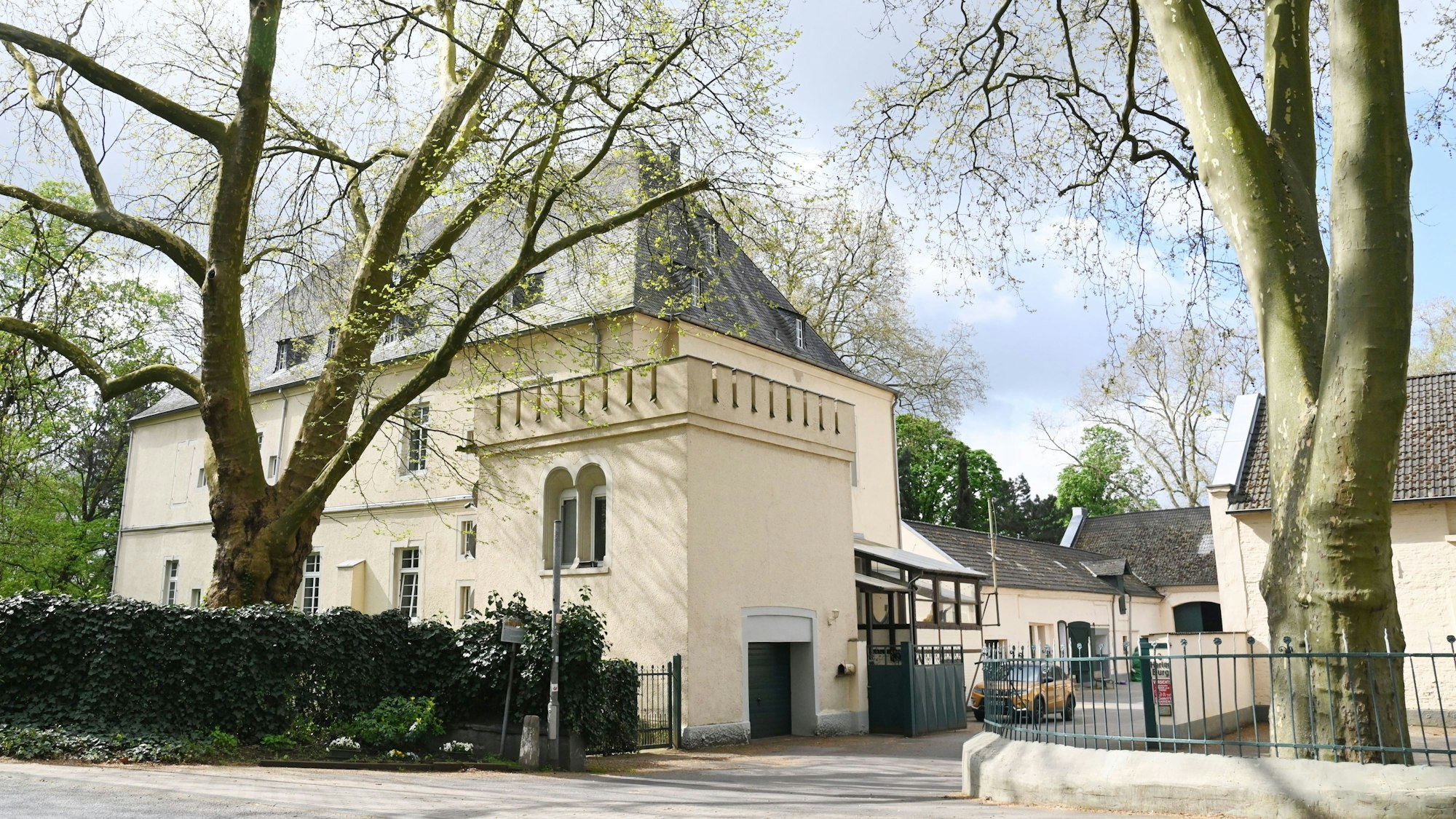 Ein großes herrschaftliches Gebäude mit Nebengebäuden und einer vergitterten Hofeinfahrt ist zu sehen.