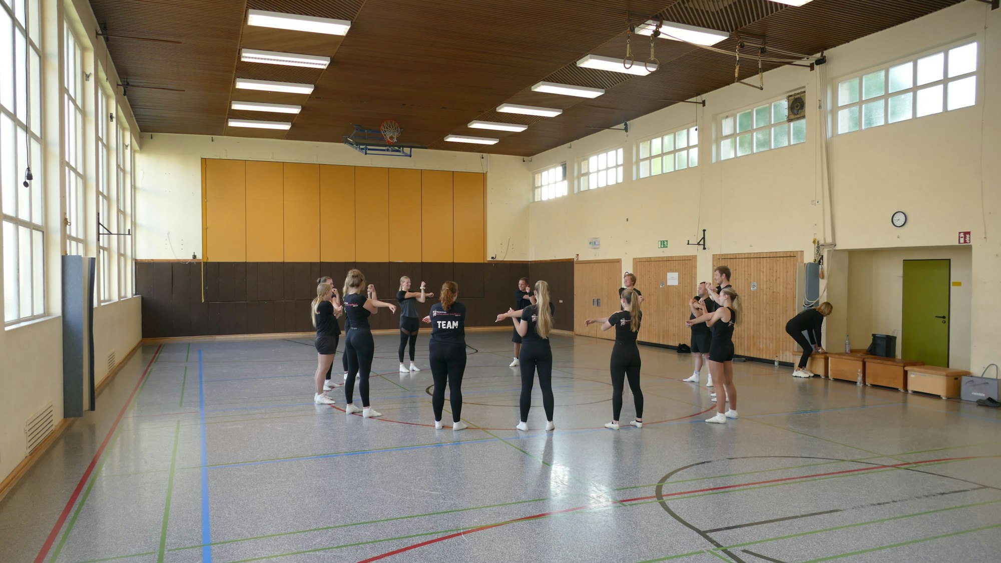 Eine alte Turnhalle, Mädchen und junge Frauen in schwarzer Trainingskleidung.