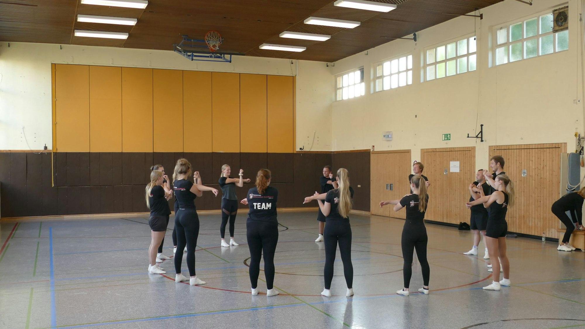 Junge Frauen in schwarzer Trainingskleidung stehen in einer Sporthalle im Kreis.