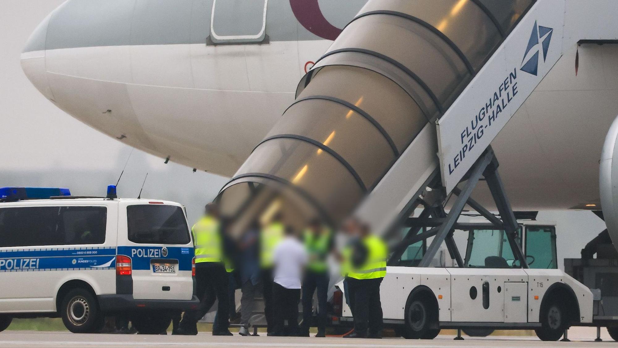 Menschen besteigen ein Flugzeug der Qatar Airways, vor dem Fahrzeuge der Bundespolizei stehen auf dem Vorfeld am Flughafen Leipzig/Halle.