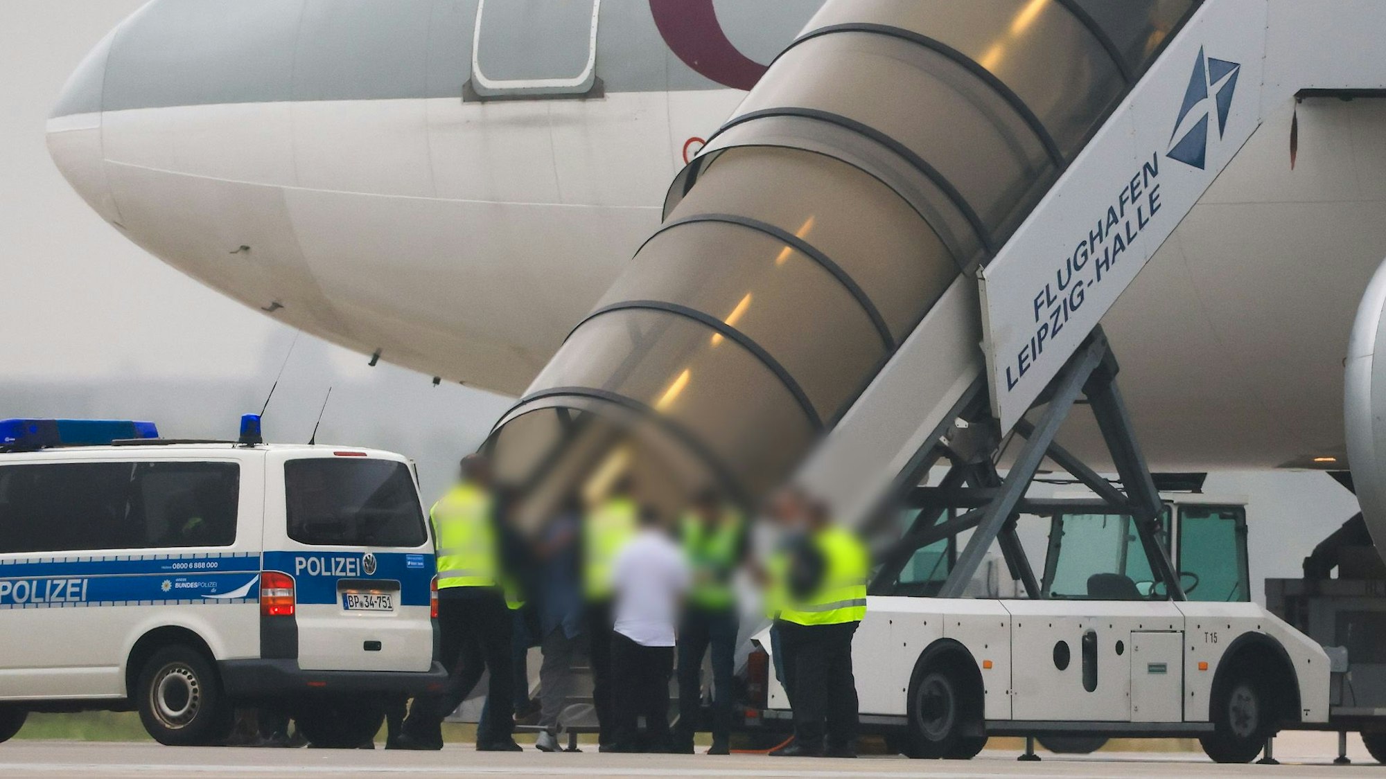 Menschen besteigen ein Flugzeug der Qatar Airways, vor dem Fahrzeuge der Bundespolizei stehen auf dem Vorfeld am Flughafen Leipzig/Halle.