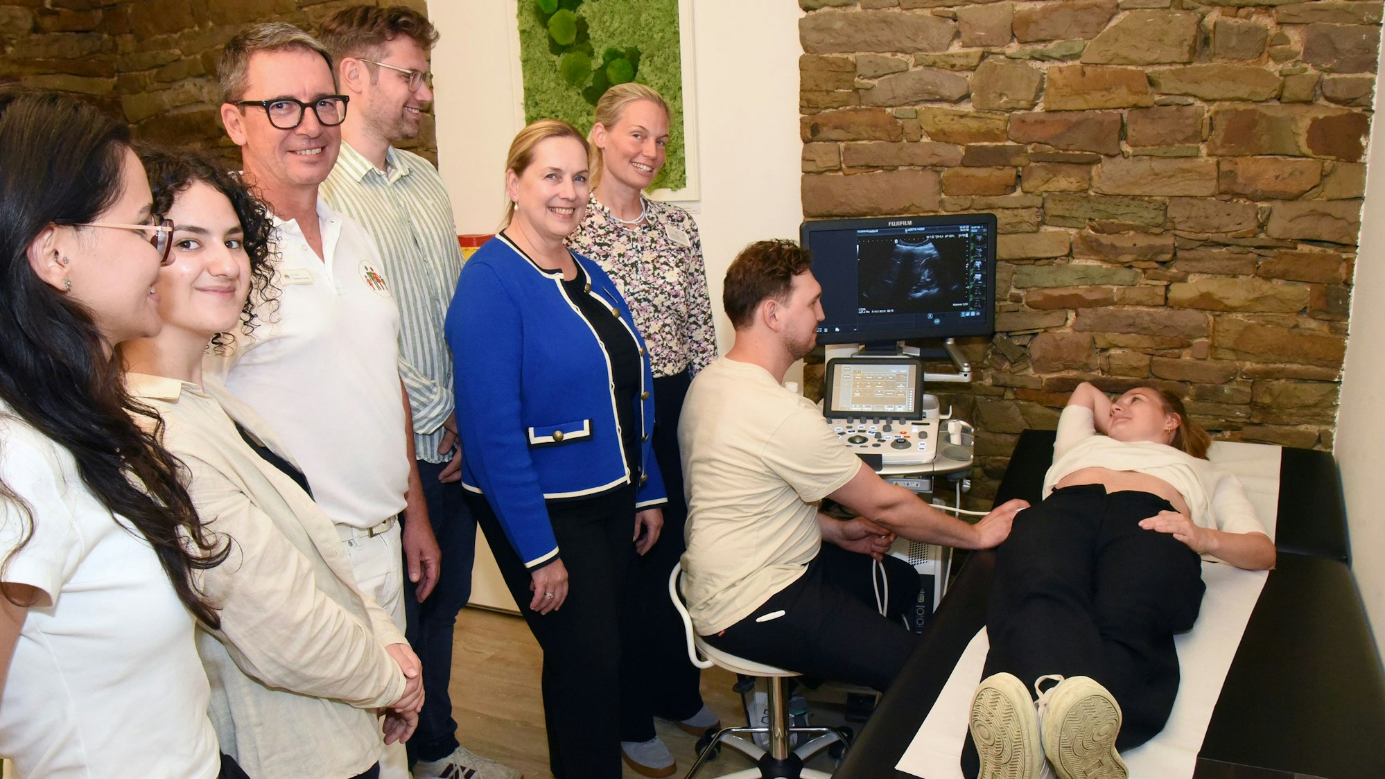 Blick auf eine Menschengruppe, die einem Studenten dabei zusieht, wie der eine Ärztin mit einem Ultraschallgerät untersucht.