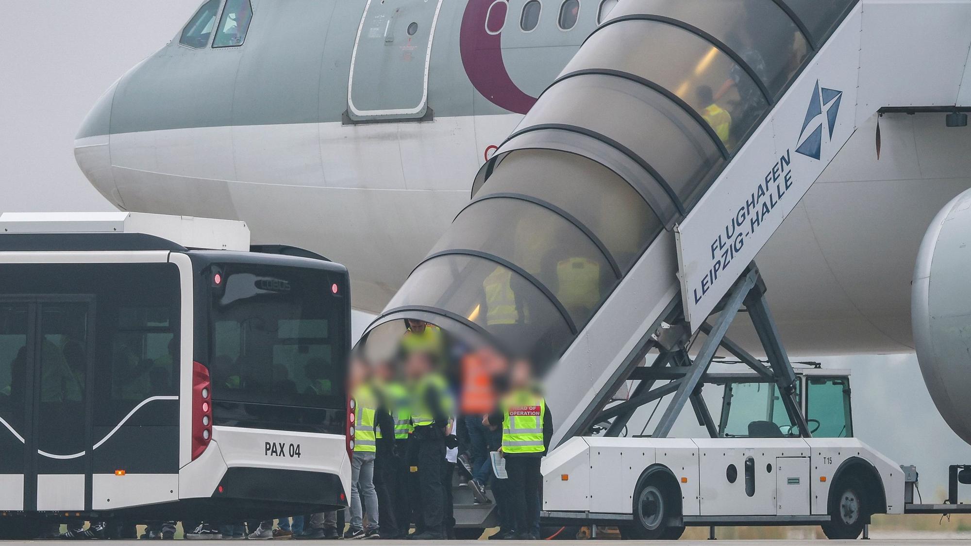 Menschen besteigen ein Flugzeug der Qatar Airways, vor dem Beamte der Bundespolizei stehen, auf dem Vorfeld am Flughafen Leipzig/Halle.