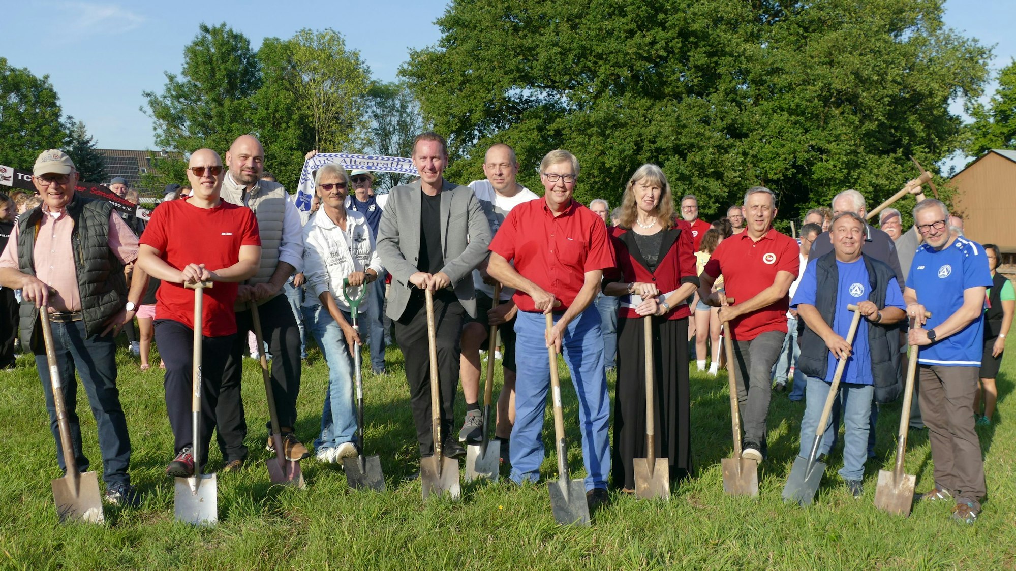 Männer und Frauen stehen mit Spaten auf einer Wiese.
