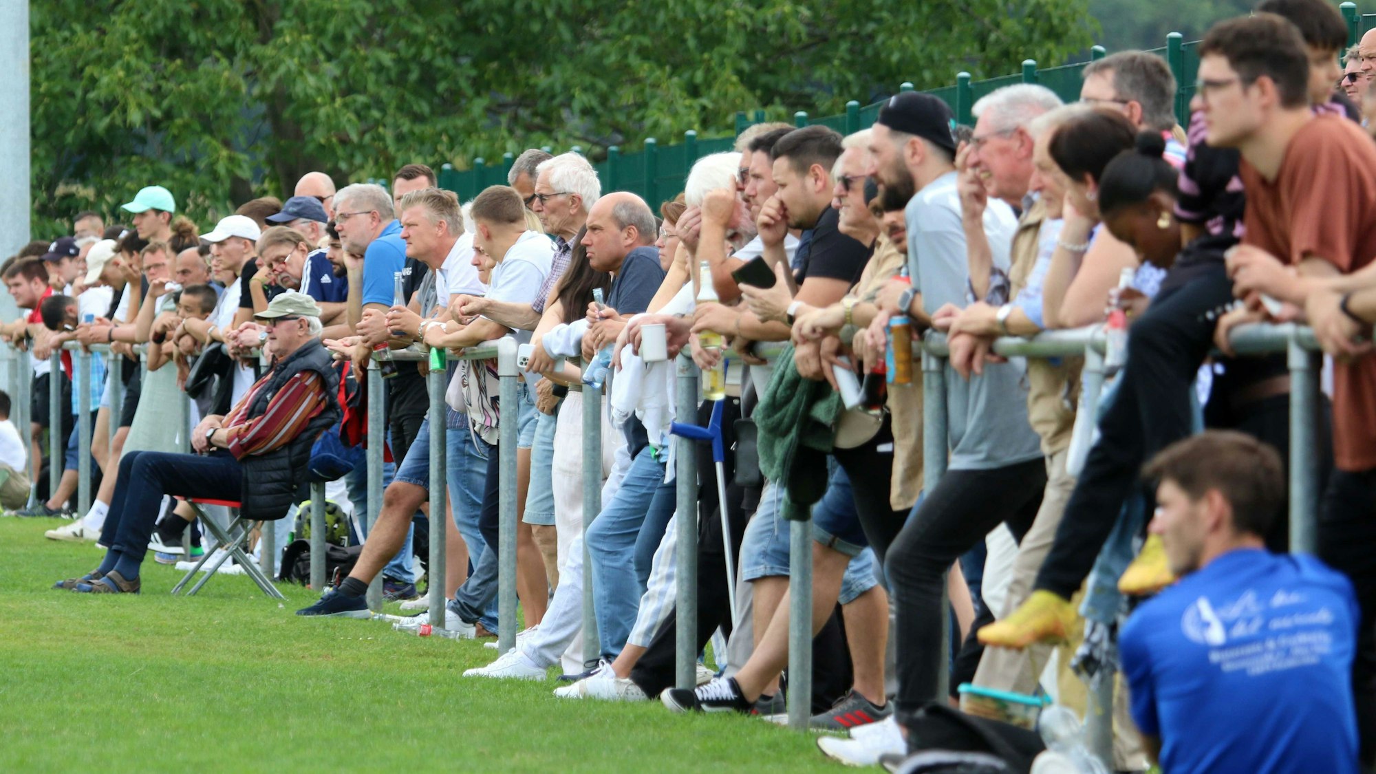 Am Spielfeldrand stehen Zuschauer hinter der Absperrung und gucken ein Fußballspiel.