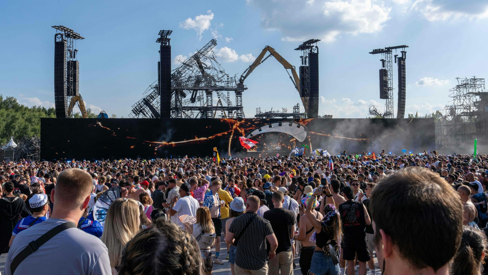 Festivalbesucher stehen am Freitag (18. Juli) vor der abgebrannten Hauptbühne des Tomorrowland-Festivals in Belgien. Nun erschüttert ein Todesfall eines der größten Techno-Festivals weltweit.
