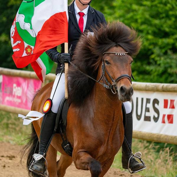 Emma Brust auf dem Rücken eines Pferdes. In der Hand hält sie eine NRW-Flagge.