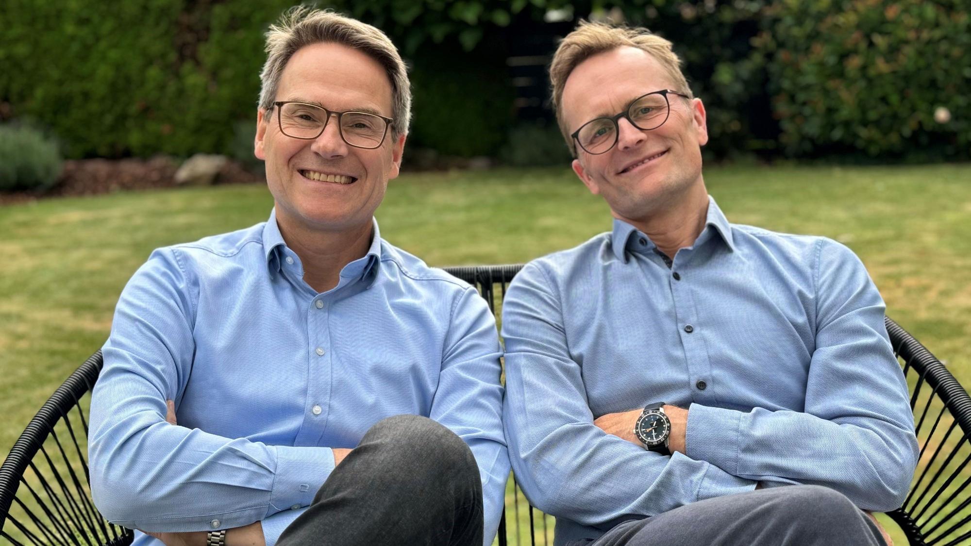 Zwei Männer, die Arme verschränkt, posieren für das Foto.