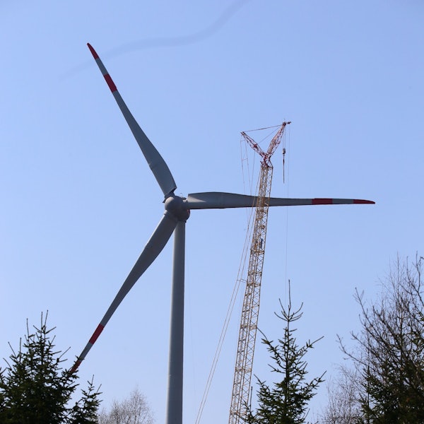 Das Bild zeigt ein Windrad, dahinter steht ein Baukran.