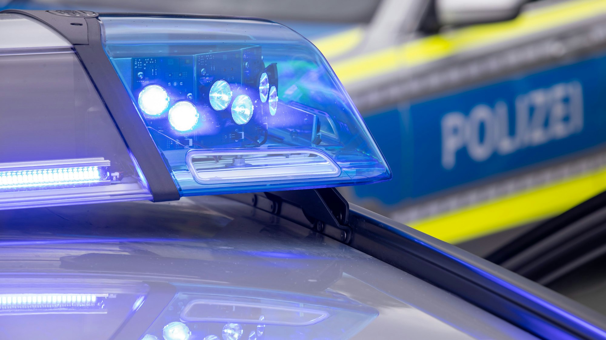 Nahaufnahme auf Blaulicht auf einem Polizeiauto: Im Hintergrund steht unscharf ein weiterer Polizeiwagen. (Symbolbild)