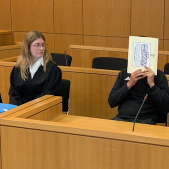 Der Angeklagte hält sich in einem Gerichtssaal in Aachen einen Aktendeckel vors Gesicht.