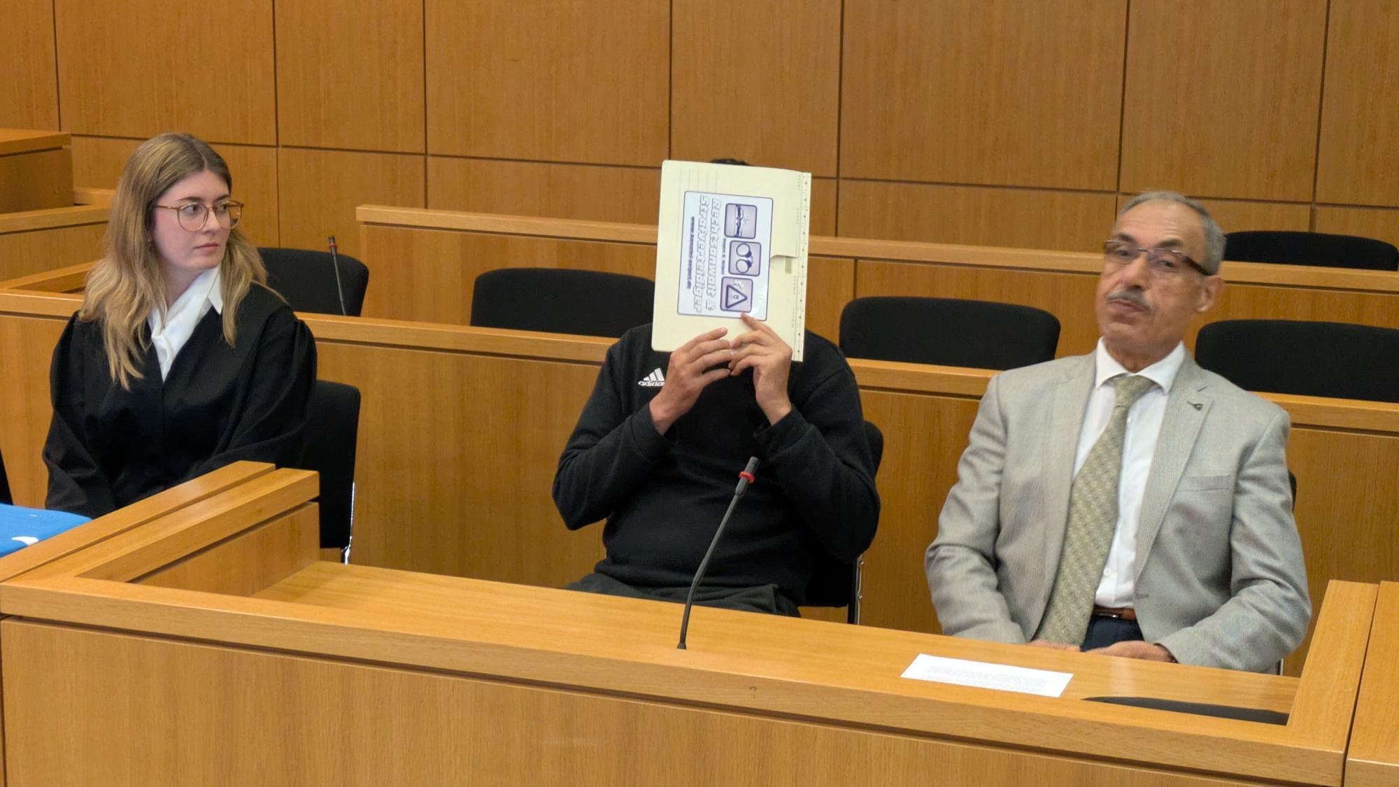 Der Angeklagte hält sich in einem Gerichtssaal in Aachen einen Aktendeckel vors Gesicht.