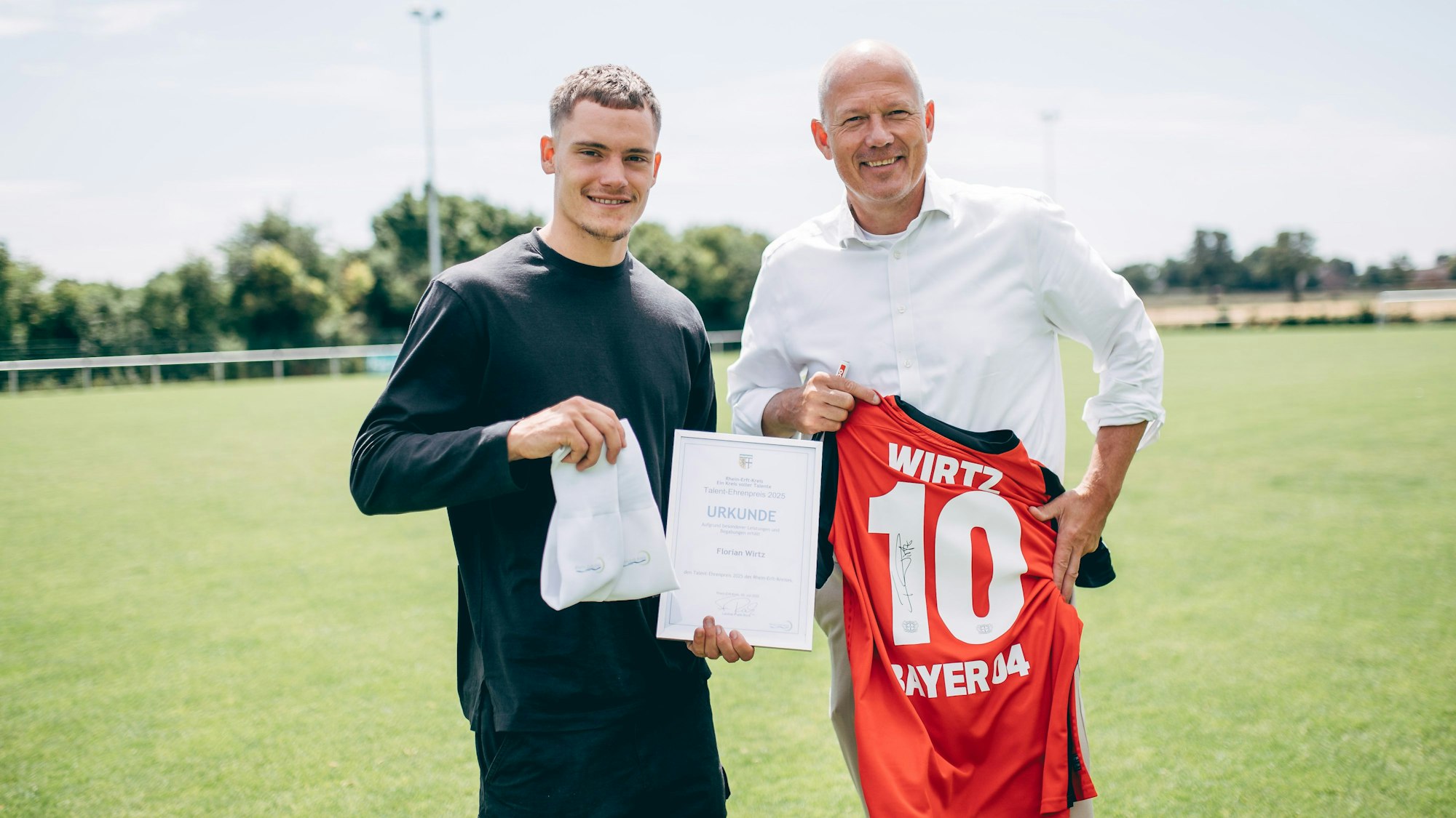Ein junger Mann (l.) hält eine Urkunde in der Hand, der ältere von beiden ein Trikot mit der Aufschrift Wirtz.