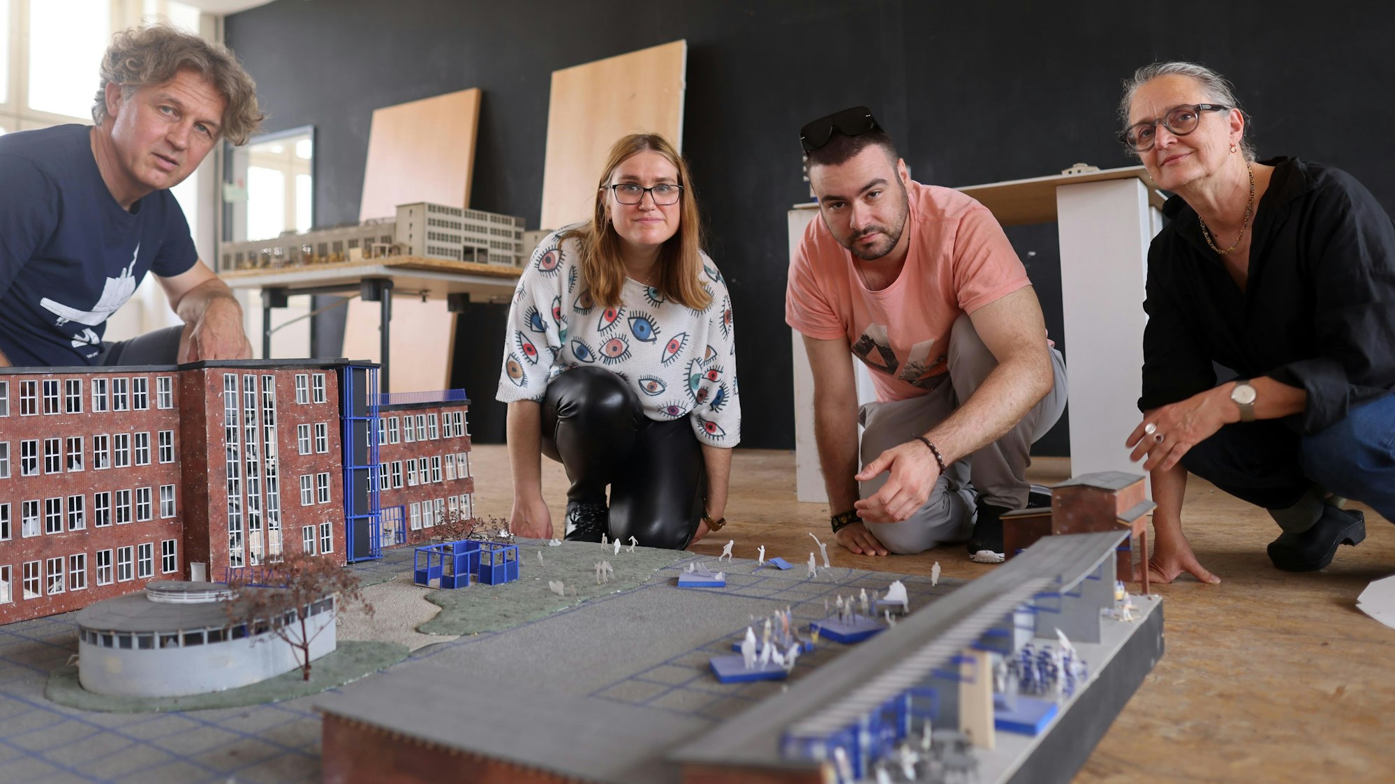 Vier Menschen vor dem Modell eines großen Gebäudes.