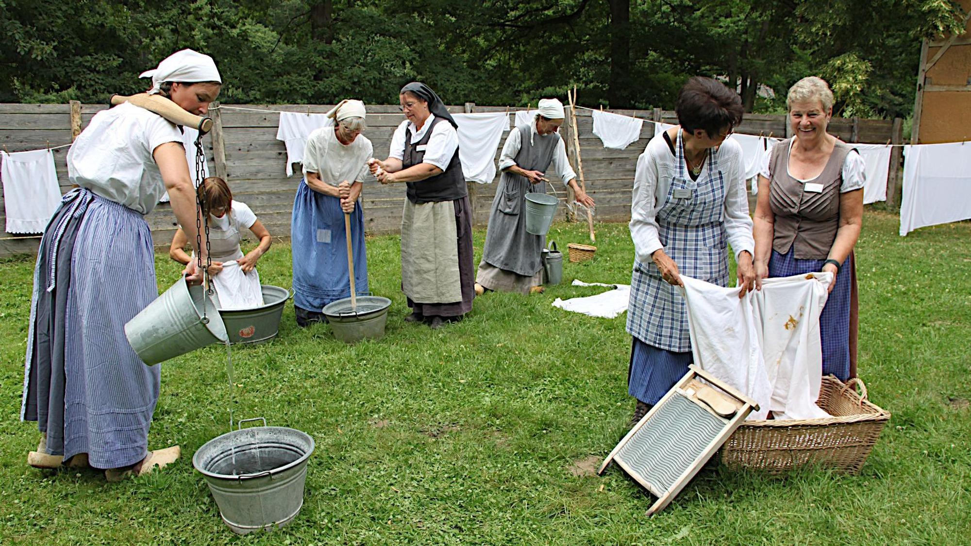 Frauen in historischer Kostümierung stehen an Waschbrettern und waschen Leinenzeug.