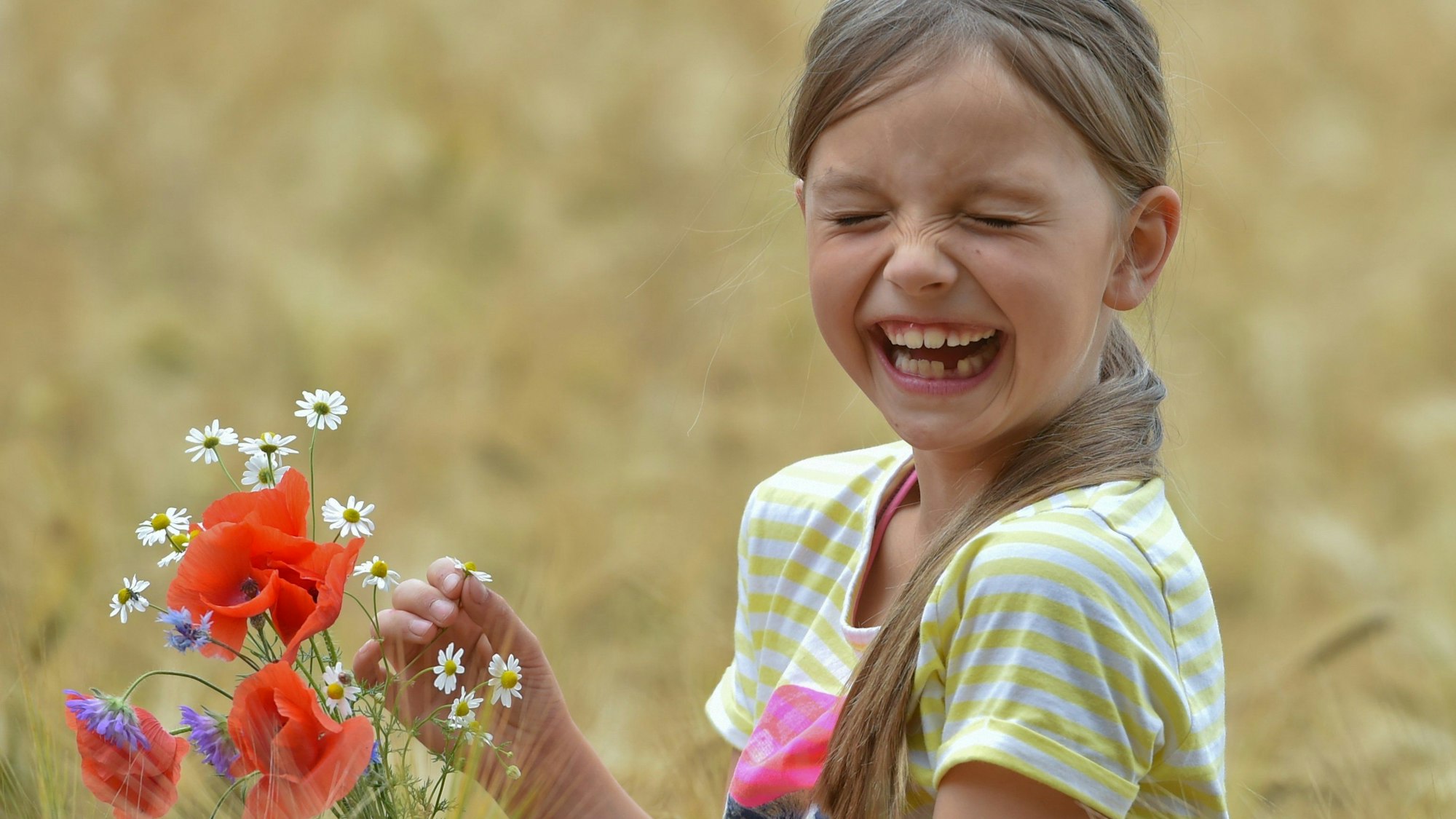 Das Bild zeigt ein lachendes Mädchen mit Blumen in einem Feld.