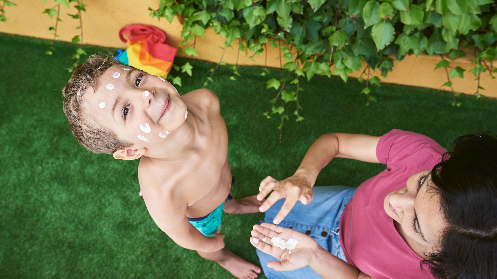 Das Bild zeigt einen Jungen, der von seiner Mutter mit Sonnencreme eingeschmiert wird.