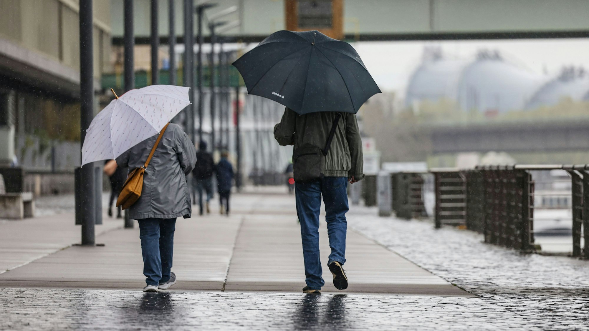 Spaziergänger gehen mit Regenschirmen am Rheinufer entlang. (Archiv)