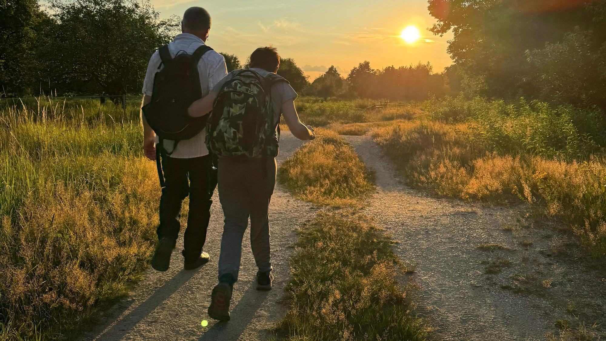 Eine Pate läuft mit seinem Patenkind bei Sonnenuntergang einen Weg entlang.