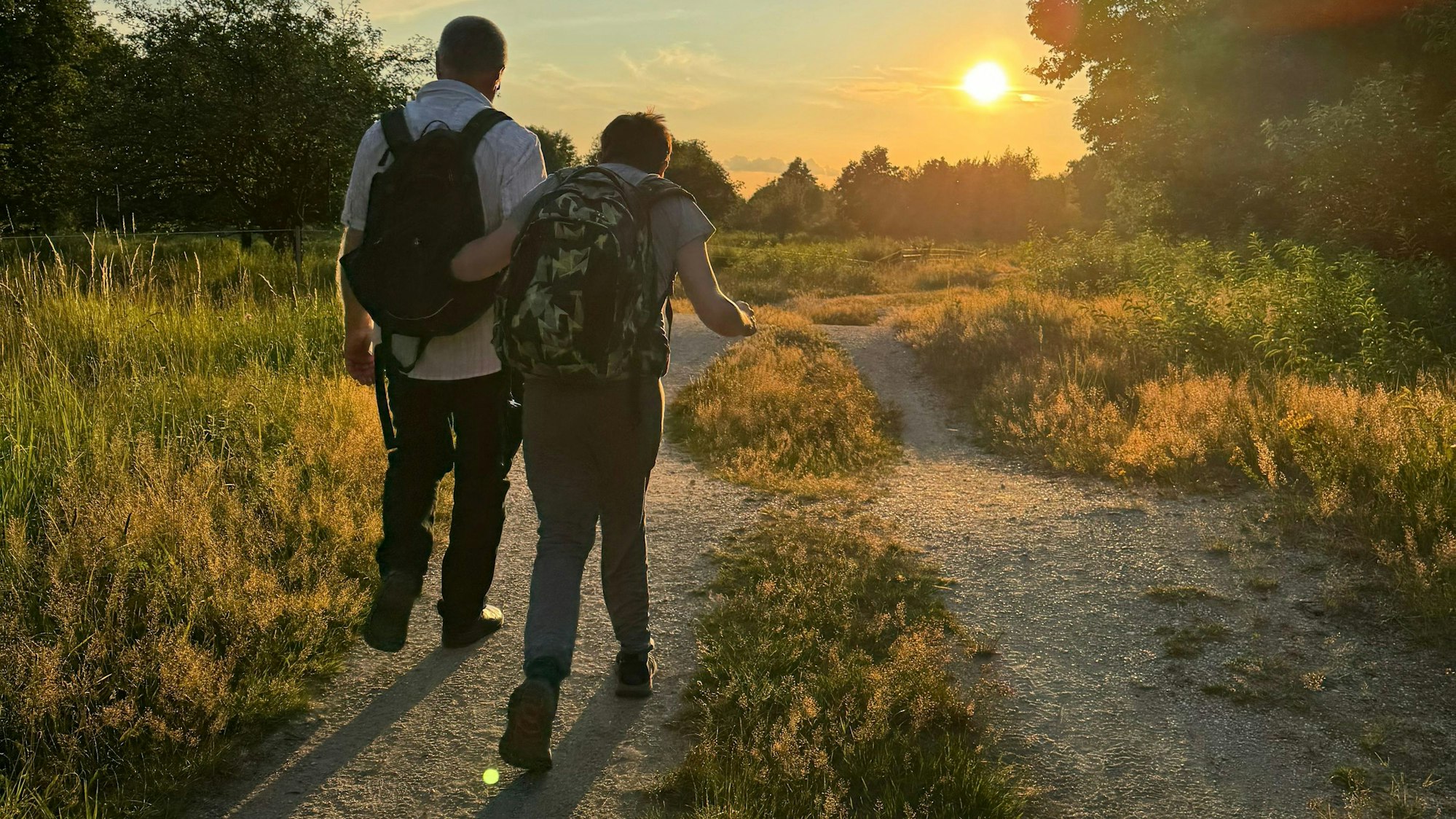 Eine Pate läuft mit seinem Patenkind bei Sonnenuntergang einen Weg entlang.