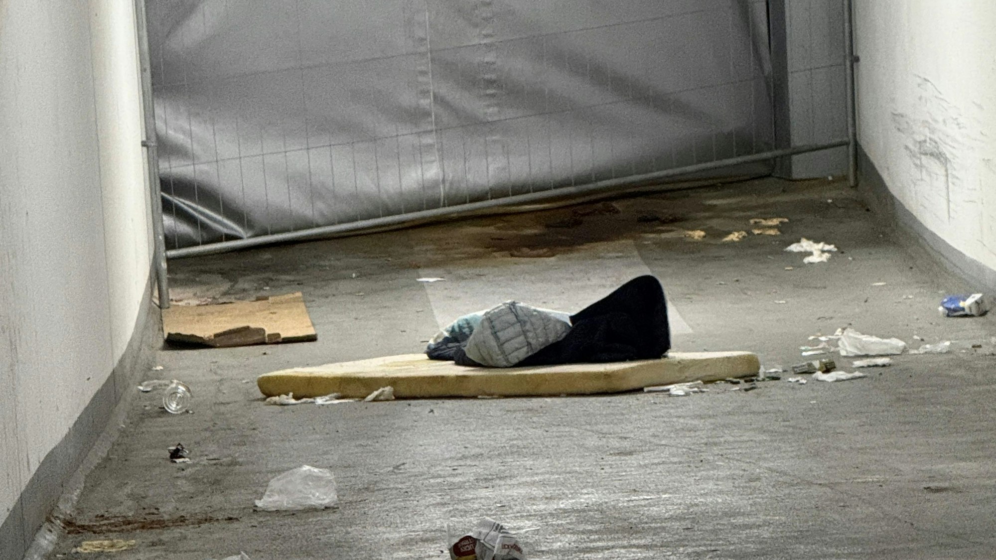 Vor einer mit einem Bauzaun abgesperrten Einfahrt sind eine kaputte Matratze, Müll und Pfützen zu sehen.