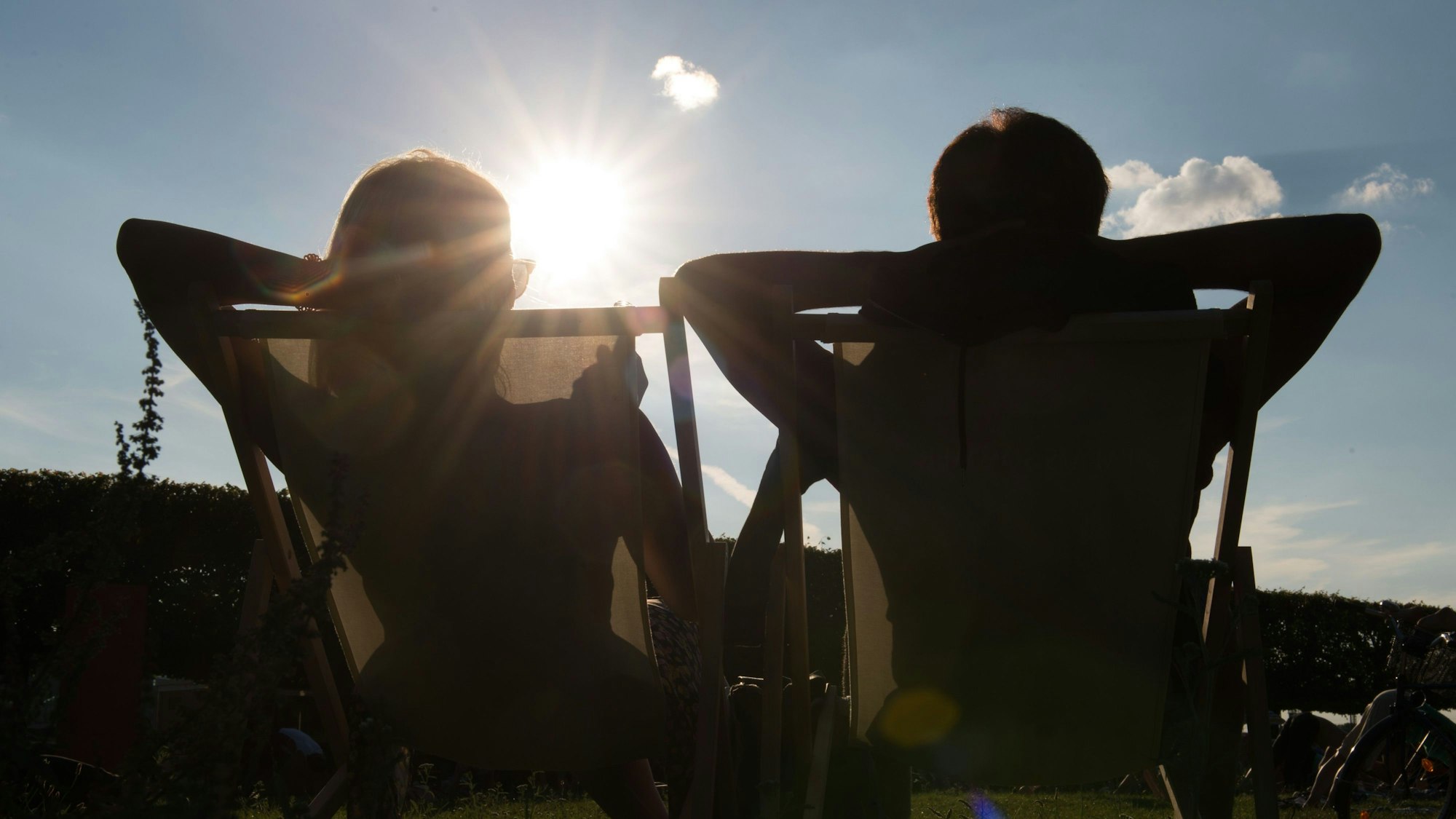 Das Bild zeigt zwei Personen in Liegestühlen, die sich sonnen.