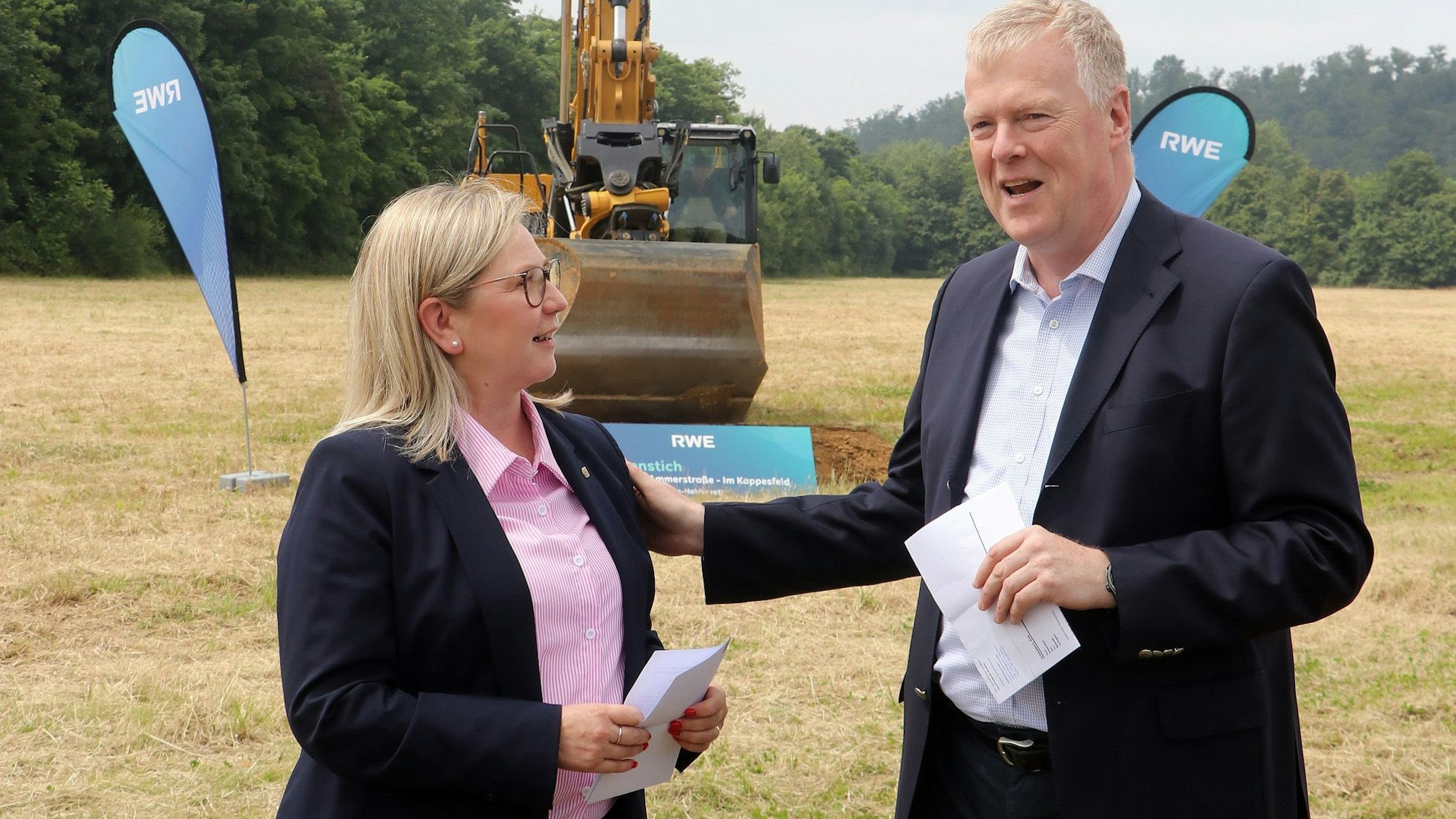 Auf dem Bild sind ein Mann und eine Frau bei einer Rede auf einem Spatenstich zu sehen.
