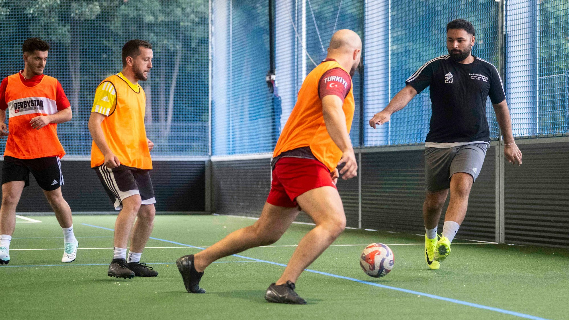 Spieler des Euskirchener TSC trainieren in einer Sporthalle das Fußballspielen. Einige tragen orangefarbene Leibchen.