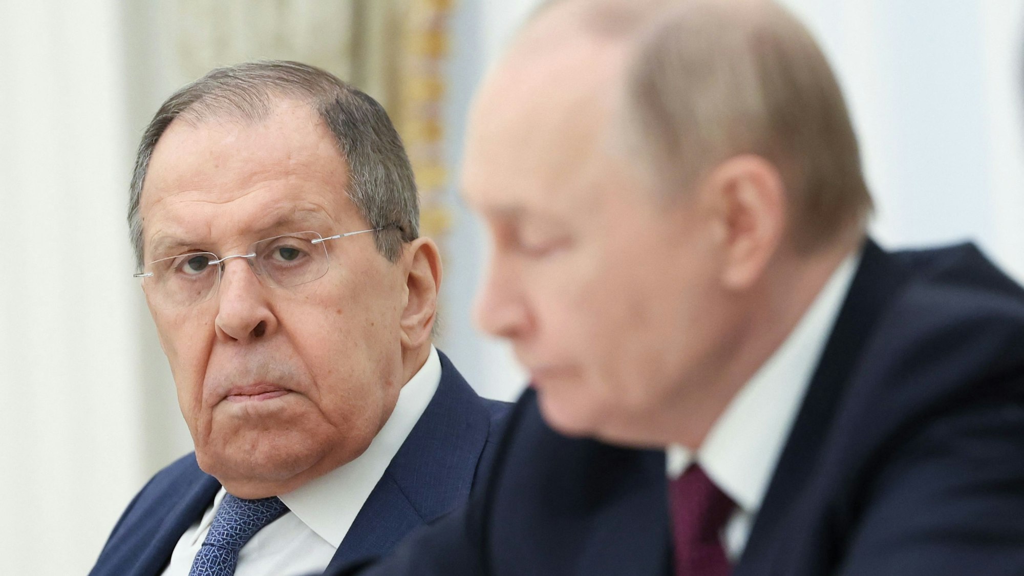 Russlands Außenminister Sergej Lawrow schaut in die Kamera. Im Vordergrund ist Kremlchef Wladimir Putin unscharf zu sehen. (Archivbild)
