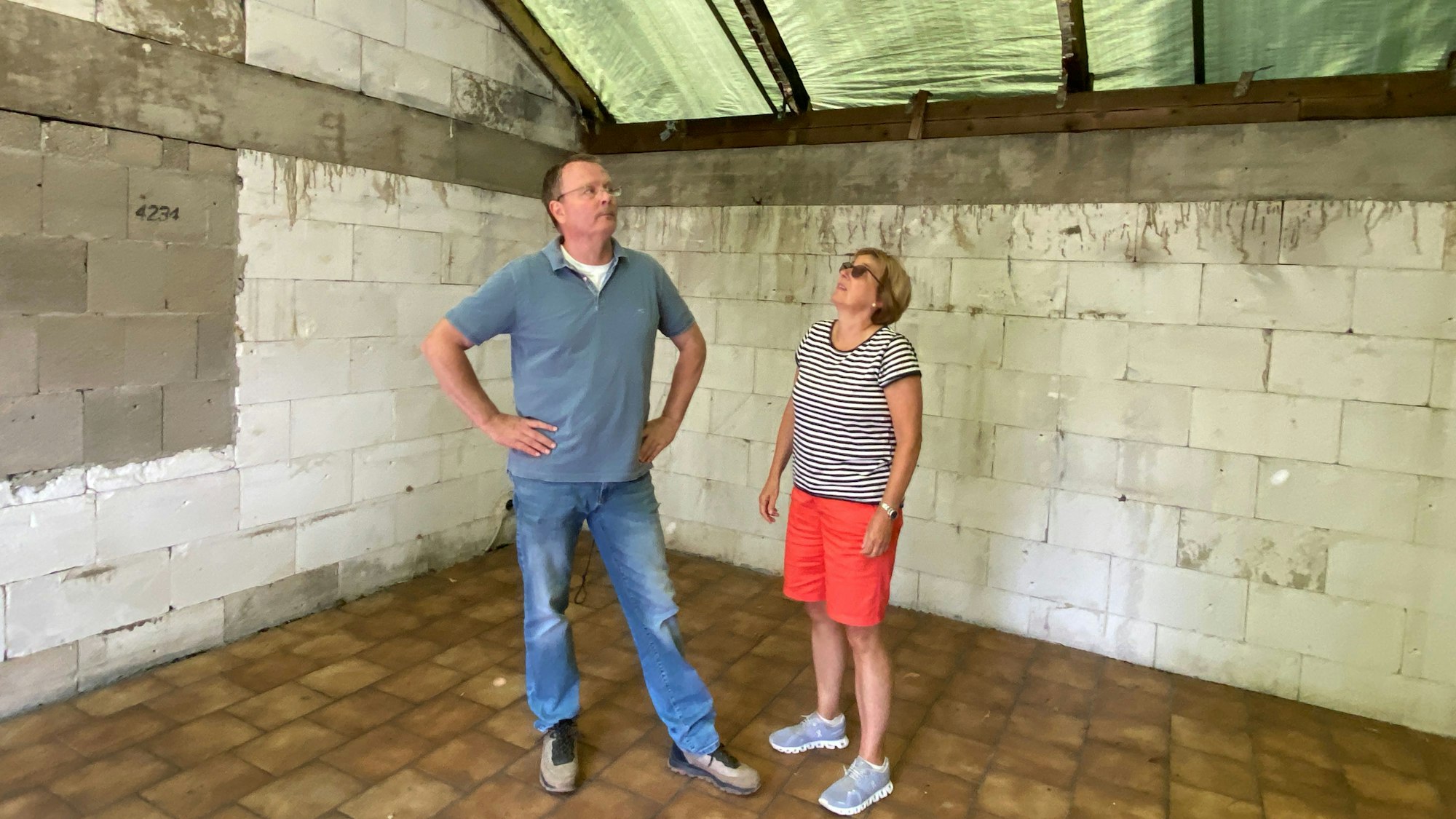 Vorsitzender Deters und Geschäftsführerin Sanders stehen im entkernten Clubhaus und schauen sich den zerstörten Dachstuhl an.