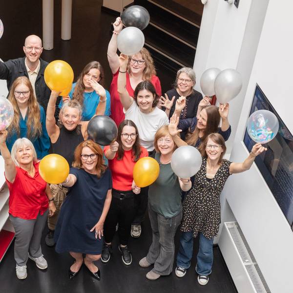 Frauen und ein Mann halten Luftballons in die Höhe. Sie freuen sich.