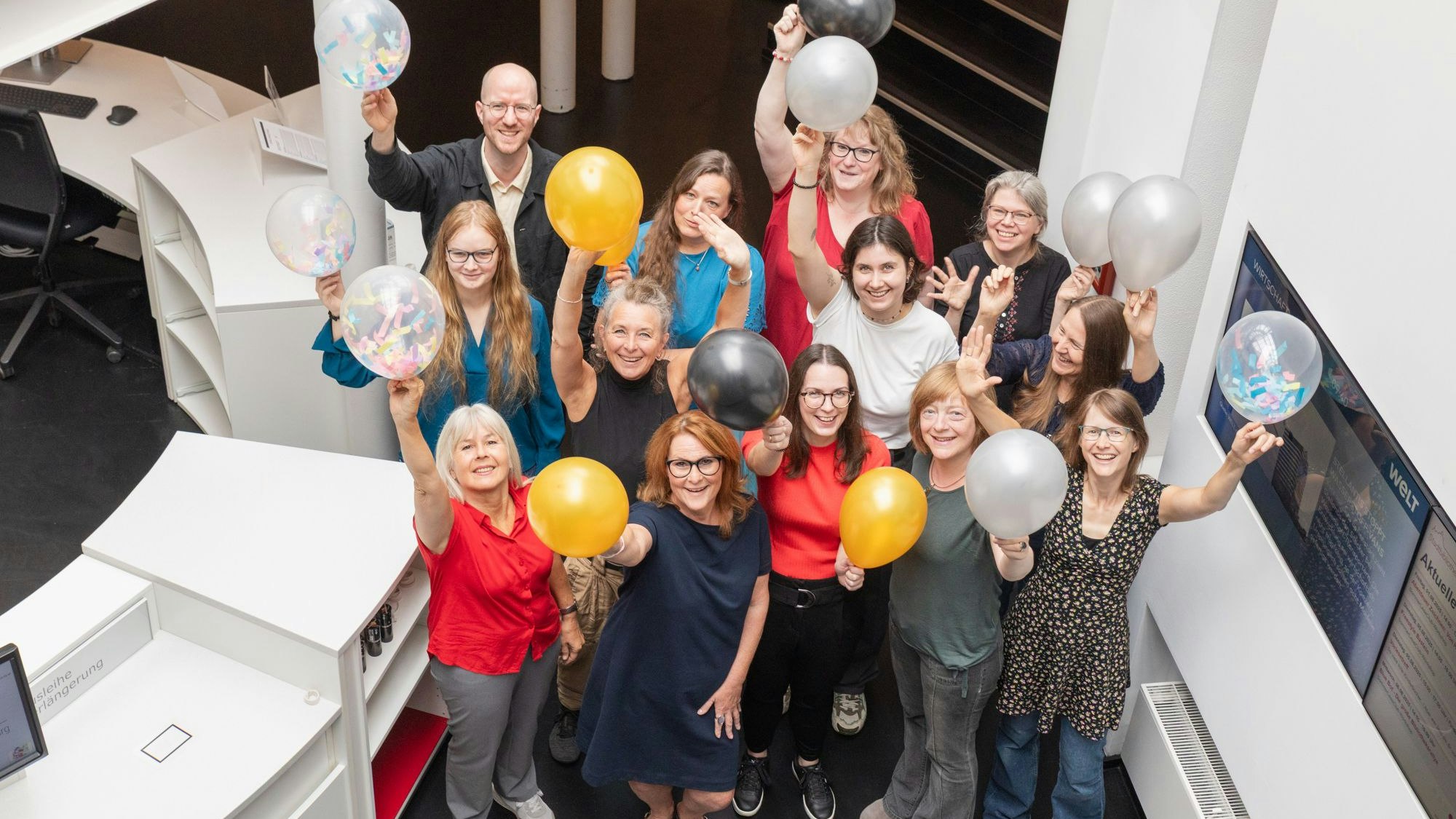 Frauen und ein Mann halten Luftballons in die Höhe. Sie freuen sich.