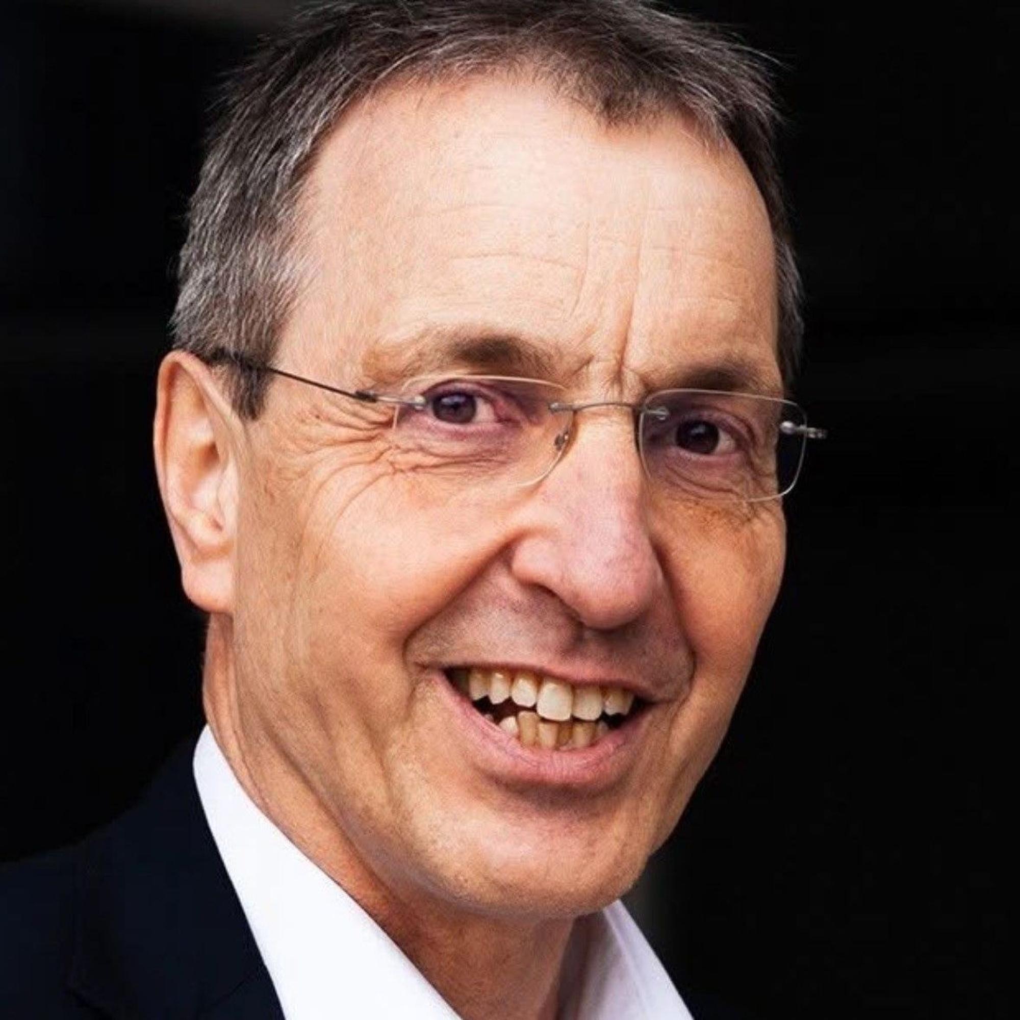 Auf dem Bild ist das Portrait von Raimund Hegwald zu sehen, er lacht in die Kamera.