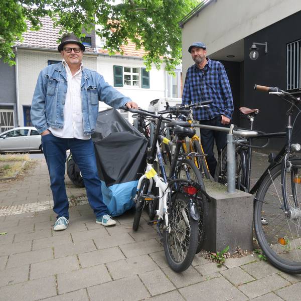 Zwei Männer stehen neben abgestellten Fahrrädern an der Rampe zum Eingang einer ehemaligen Postfiliale.