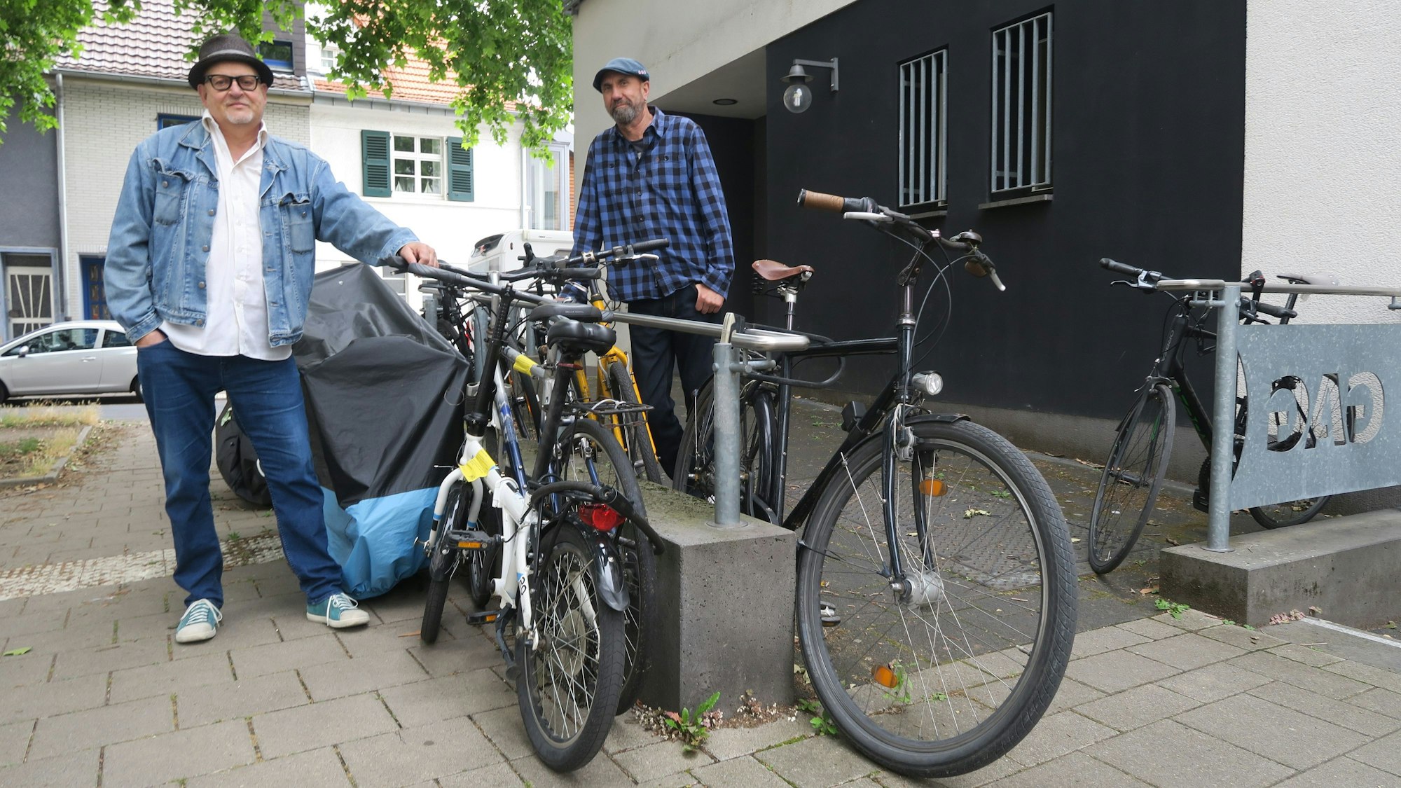 Zwei Männer stehen neben abgestellten Fahrrädern an der Rampe zum Eingang einer ehemaligen Postfiliale.