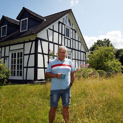 Ein Mann mit Kaffeebecher vor einem Fachwerkhaus.
