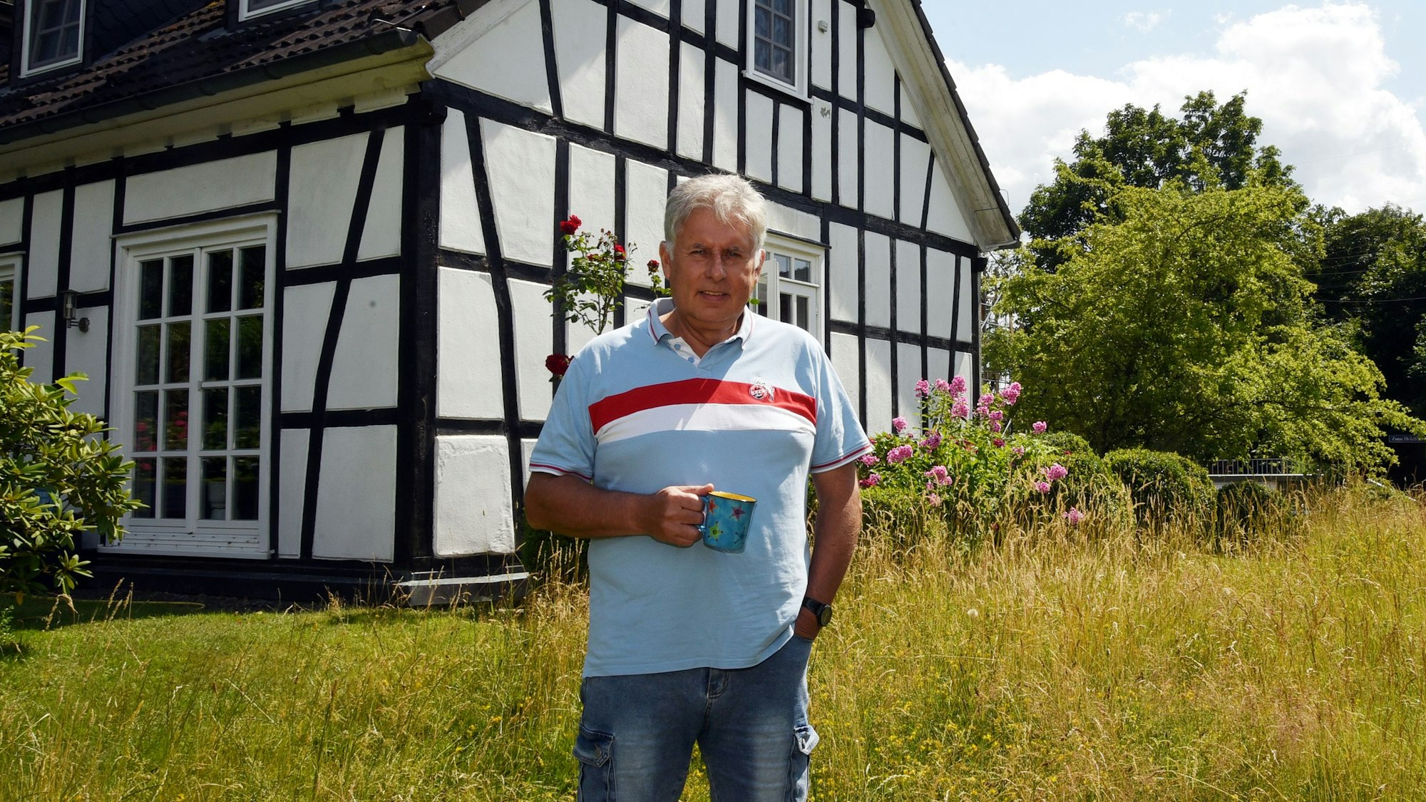 Ein Mann mit Kaffeebecher vor einem Fachwerkhaus.