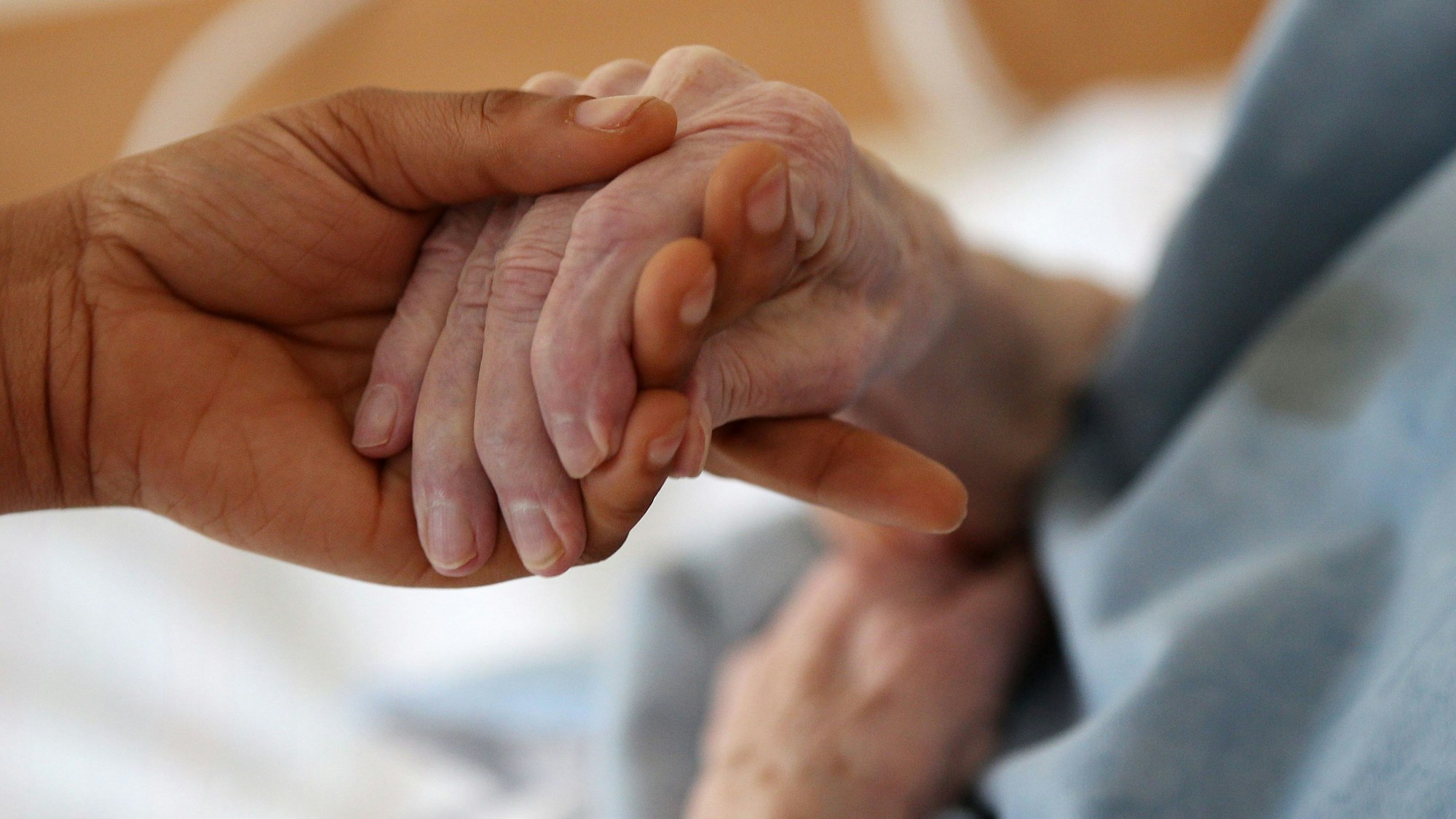 Eine jüngere Frau hält die Hand einer Seniorin.