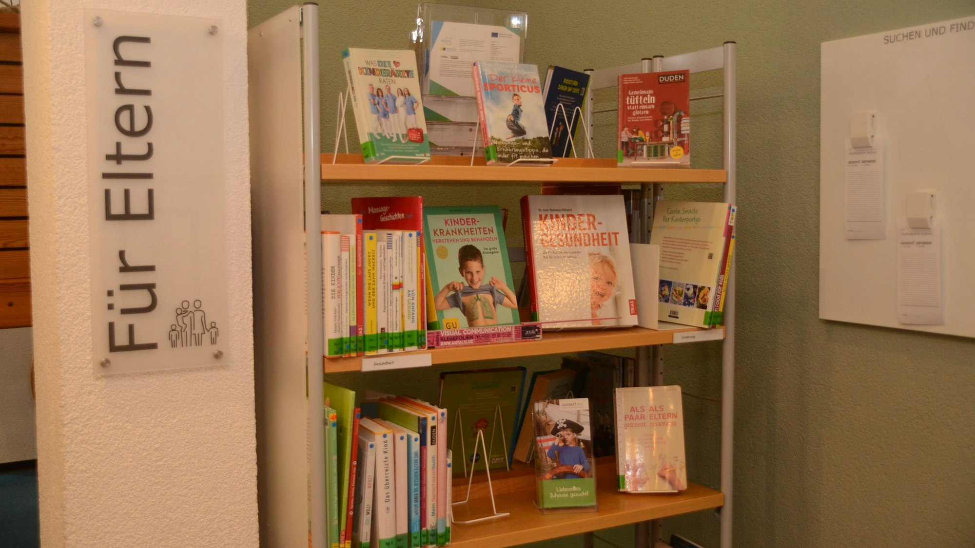 Ein Regal in einer Bibliothek. Auf einem weißen Schild steht "für Eltern".