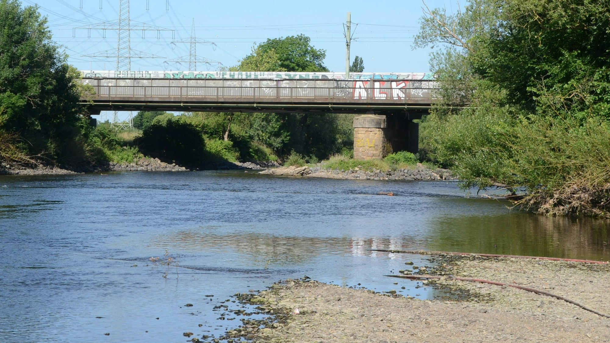Eine Brücke über einen kleinen Fluss. Der Wasserstand ist niedrig, das Kiesufer ist breit.