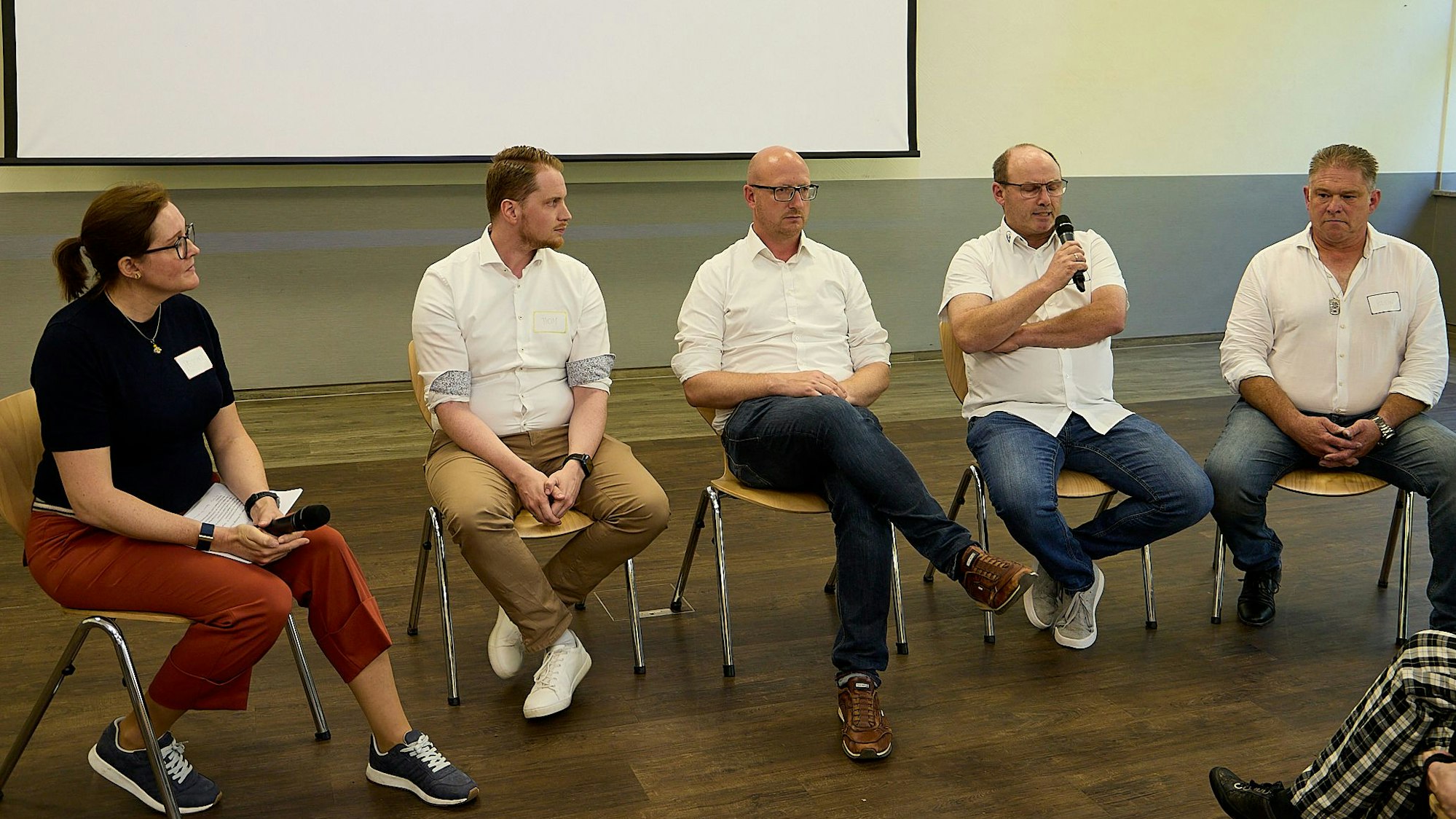 Jürgen Klein, Ralph Loehr, Ingo Pfennings, Manuel Thom und Moderatorin Melanie Peschel sitzen nebeneinander auf Stühlen vor einer Leinwand.
